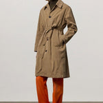 Front view of beige mustang trench on model wearing orange pants and boots, against a white background.
