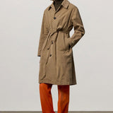 Front view of beige mustang trench on model wearing orange pants and boots, against a white background.