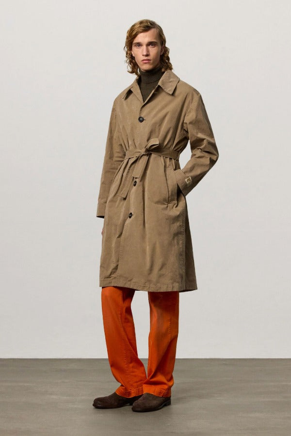 Front view of beige mustang trench on model wearing orange pants and boots, against a white background.