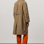 Back view of beige mustang trench on model wearing orange pants and boots, against a white background.