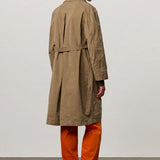 Back view of beige mustang trench on model wearing orange pants and boots, against a white background.