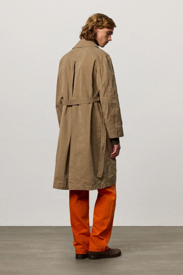 Back view of beige mustang trench on model wearing orange pants and boots, against a white background.