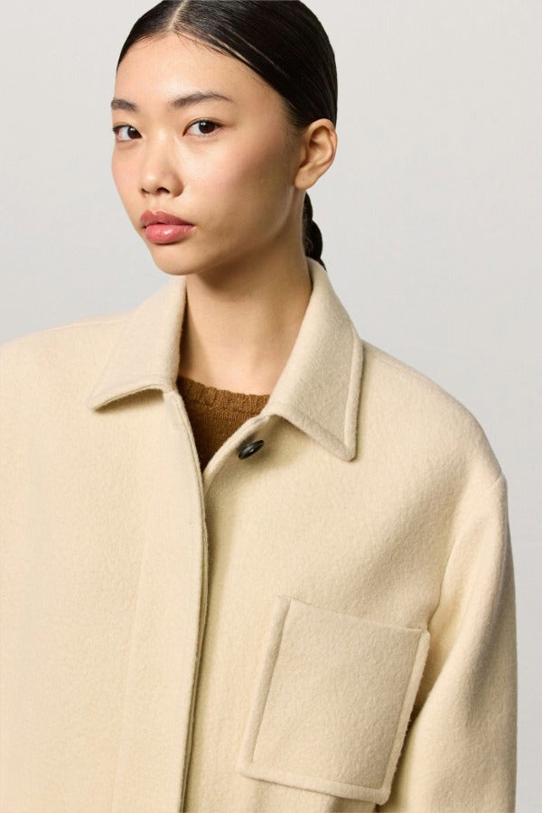 Front closeup view of milk rouen jacket on model wearing tan sweater, against a white background.