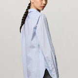 Back view of azzurro uma classic shirt on modeh wearing grey pants, against a white background.
