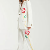 Side view of off white button embroidered sb jacket on model wearing matching pants and sneakers, against a white background.
