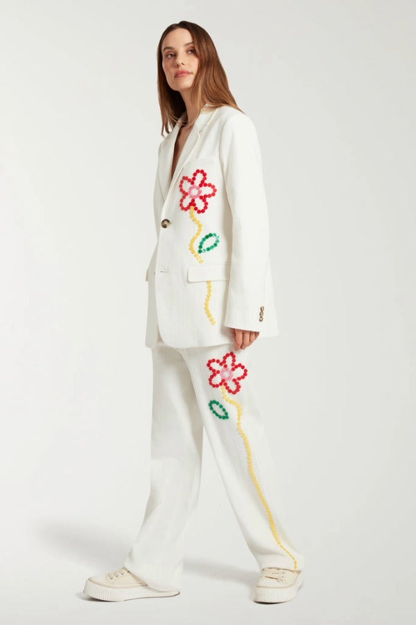 Side view of off white button embroidered sb jacket on model wearing matching pants and sneakers, against a white background.