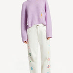 Front view of lilac embroidered sweater on model wearing white denim and sneakers, against a white background.