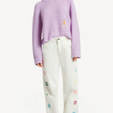 Front view of lilac embroidered sweater on model wearing white denim and sneakers, against a white background.
