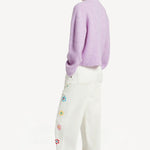 Back view of lilac embroidered sweater on model wearing white denim and sneakers, against a white background. 