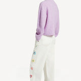 Back view of lilac embroidered sweater on model wearing white denim and sneakers, against a white background. 
