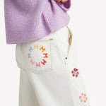 Side closeup view of lilac embroidered sweater on model wearing white denim, against a white background.