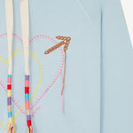 Front closeup view of pale blue embroidered heart hoodie on white background, with no model shown.