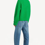 Back view of denim embroidered scribble jean on model wearing green sweater and pink slides, against a white background.