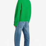 Back view of denim embroidered scribble jean on model wearing green sweater and pink slides, against a white background.