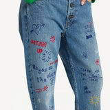 Front closeup view of denim embroidered scribble jean on model wearing green sweater, against white background