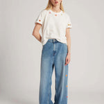Front view of mid blue embroidered straight leg jean on model wearing white t-shirt and whiter sneakers, against a white background.