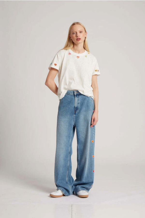 Front view of mid blue embroidered straight leg jean on model wearing white t-shirt and whiter sneakers, against a white background.