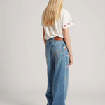 Back view of mid blue embroidered straight leg on model wearing white t-shirt and white sneakers, against white background.