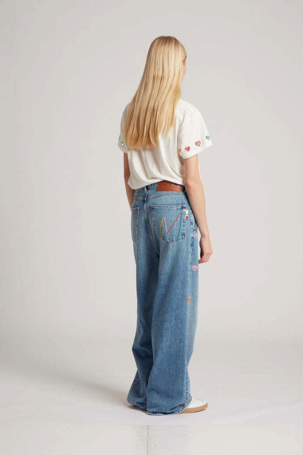 Back view of mid blue embroidered straight leg on model wearing white t-shirt and white sneakers, against white background.