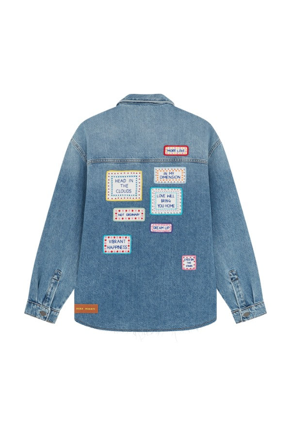 Back view of mid blue embroidered word patch denim overshirt on white background, with no model shown.