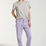 Front view of lilac garment dyed jeans on model wearing grey shirt with hearts and white sneakers, against white background.