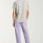 Back view of lilac garment dyed jeans on model wearing grey shirt with hearts and white sneakers, against a white background.