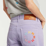 Back closeup view of lilac garment dyed jeans on model wearing grey shirt with hearts, against a white background.