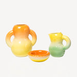 Front view of orange hand sprayed ombre vase aligned with other home goods, against a white background, with no model shown.