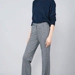 Front slanted view of navy blue herringbone paris pant on model wearing navy top and sneakers, against a grey background.