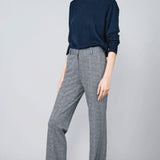 Front slanted view of navy blue herringbone paris pant on model wearing navy top and sneakers, against a grey background.