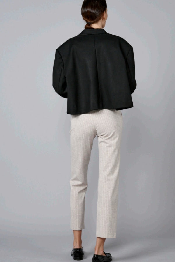 Back view of beige striped universal pant on model wearing black jacket and loafers, against a grey background.