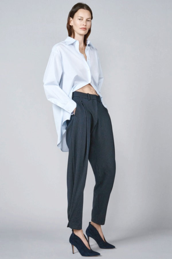 Front view of navy pinstriped jersey sarouel pant on model wearing blue shirt and heels, against a grey background.