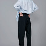Back view of navy pinstriped jersey sarouel pant on model wearing blue shirt and heels, against a grey background.