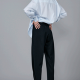 Back view of navy pinstriped jersey sarouel pant on model wearing blue shirt and heels, against a grey background.