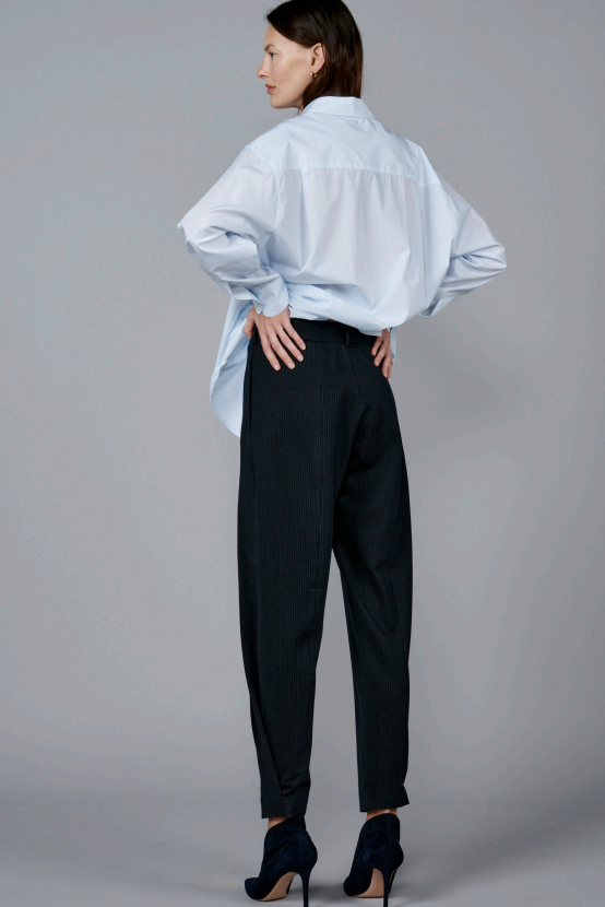 Back view of navy pinstriped jersey sarouel pant on model wearing blue shirt and heels, against a grey background.