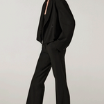 Side view of black the jacket on model wearing black pants and heels, against a white background