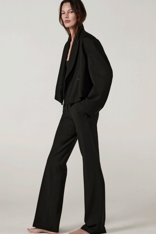 Side view of black the jacket on model wearing black pants and heels, against a white background