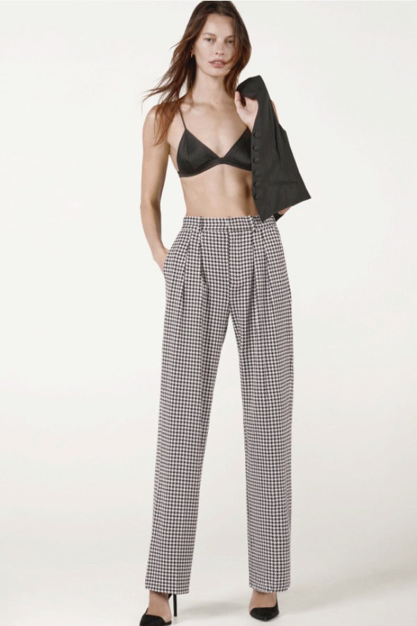 Front view of black and white houndstooth jersey long legged pant on model wearing black bra and heels, against a white background.