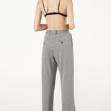Back view of black and white houndstooth jersey long legged pant on model wearing black bra and heels, against a white background.
