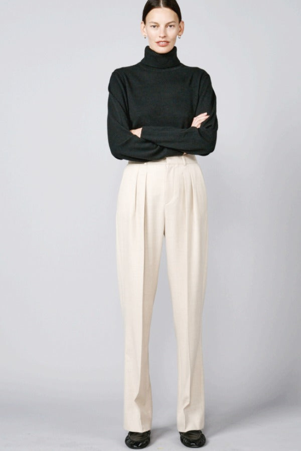 Front view of creme long legged pant on model wearing black sweater and loafers, against a grey background.