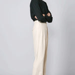 Side view of creme long legged pant on model wearing black sweater and loafers, against a grey background.