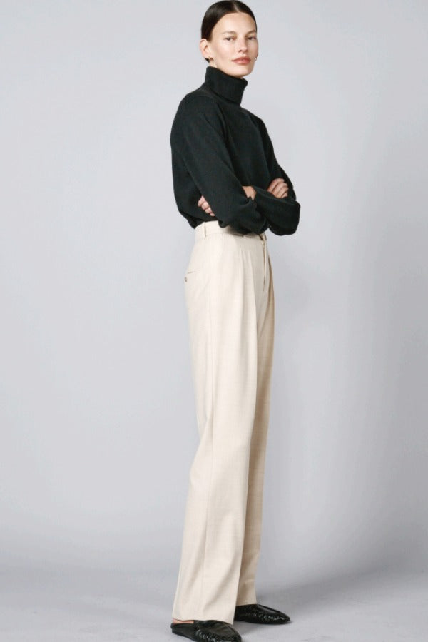 Side view of creme long legged pant on model wearing black sweater and loafers, against a grey background.