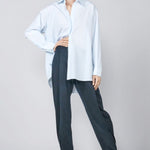 Front view of blue the shirt on model wearing navy trousers and heels, against a grey background.
