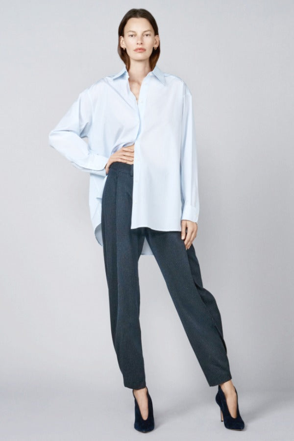 Front view of blue the shirt on model wearing navy trousers and heels, against a grey background.