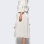 Side view of white fiesta shirt dress on model wearing beige heels, against a white background.