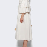 Side view of white fiesta shirt dress on model wearing beige heels, against a white background.
