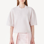 Front view of nude cashmere cropped t-shirt on model wearing pink skirt, against a white background.