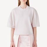 Front view of nude cashmere cropped t-shirt on model wearing pink skirt, against a white background.