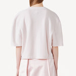 Back view of nude cashmere cropped t-shirt on model wearing pink skirt, against a white background.