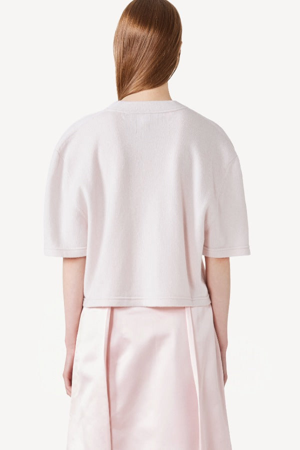 Back view of nude cashmere cropped t-shirt on model wearing pink skirt, against a white background.